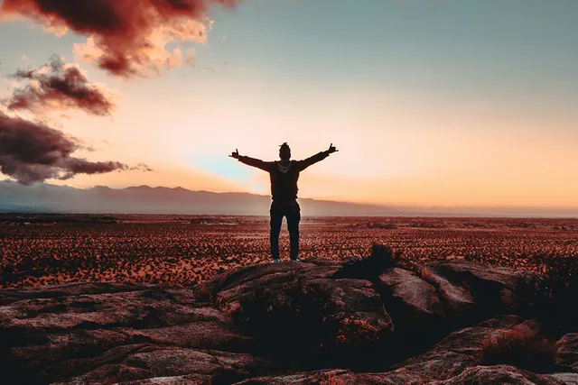 Silhouette of person reaching mountain summit at sunrise
